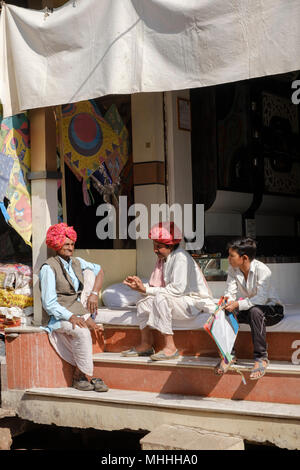 Zwei Männer in traditionellen roten Turbane und ein Junge außerhalb ihrer Shop sitzen. Bundi, Rajasthan. Indien Stockfoto