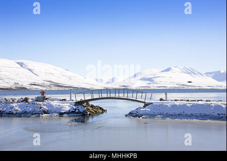 Die Fußgängerbrücke in Akureyri, Island Eyjafjordur, der längste Fjord, mit schneebedeckten Bergen im Hintergrund Stockfoto