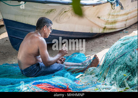 Ein Fischer mends Netze sitzt neben seinem Boot. Mann mit zurück zu Kamera arbeitet mit Nähen implementiert, Instandsetzung der Fischernetze, Galle, Sri Lanka Stockfoto