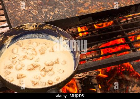 Emaillierte Pfanne auf Feuer. Vorbereitung des Pilzes Steak Sauce. Feuer im Lager Stockfoto