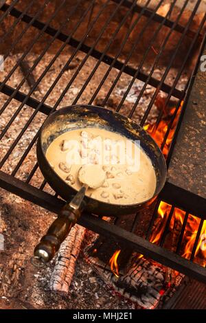 Emaillierte Pfanne auf Feuer. Vorbereitung des Pilzes Steak Sauce. Feuer im Lager Stockfoto