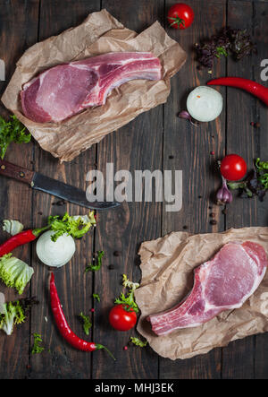 Ansicht von oben frisches rohes Schweinefleisch Hals Steak mit Gewürzen auf den Kraftpapier auf dem dunklen Hintergrund mit Gemüse und anderen Zutaten. Stockfoto