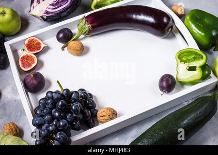 Frische organische Rohstoffe grün und violett gefärbt Gemüse und Früchte in Weiß Fach auf Stein Hintergrund. Copyspace. Stockfoto