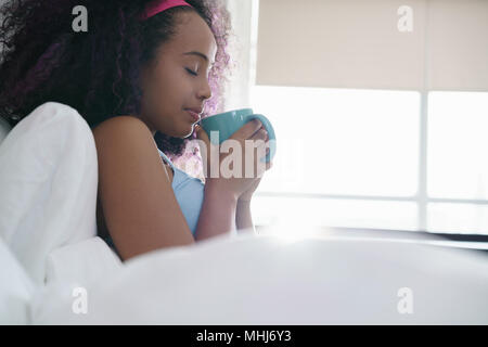 Schwarze Frau trinkt Kaffee im Bett Lächeln Stockfoto