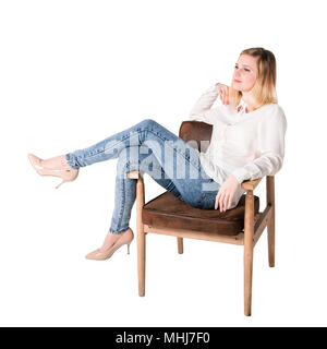 Junge schöne Frau sitzt auf einem Stuhl über so etwas nachgedacht. Jeans und weiße Bluse. Auf weiß Isoliert Stockfoto