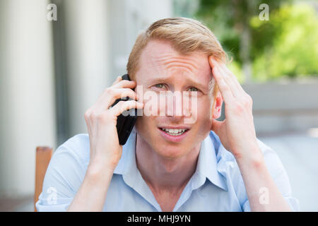 Closeup Portrait, besorgt, junger Mann im blauen Hemd am Telefon sprechen zu jemand, düster, isoliert im Freien außerhalb Hintergrund Stockfoto