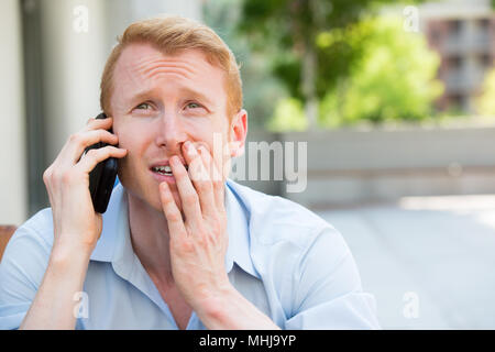 Closeup Portrait, besorgt, junger Mann im blauen Hemd am Telefon sprechen zu jemand, düster, isoliert im Freien außerhalb Hintergrund Stockfoto