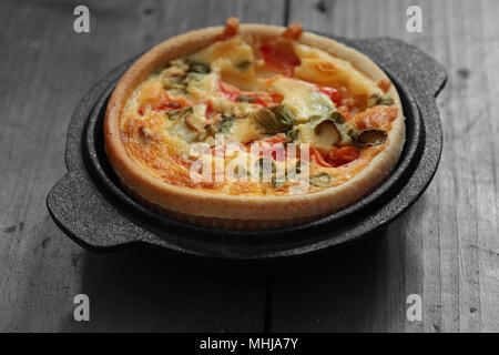 Tomaten und Frühlingszwiebel quiche in einem gusseisernen Topf, Teller auf einem Holz Hintergrund durch selektive Farbkorrektur Stockfoto