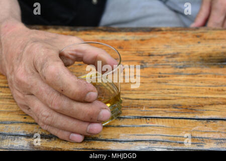 Des Menschen Hand Glas mit alten, guten Pflaumenschnaps auf alten, grunge Eiche Tisch Stockfoto