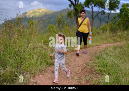 Junge Kind vor der Mutter, die auf einem Schotterweg, Mount Stuart Wanderwege, Townsville, Queensland, Australien Stockfoto