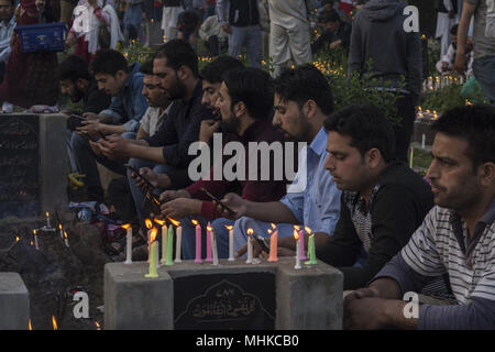 Srinagar, Jammu und Kaschmir, Indien. Mai, 2018. Kaschmir schiitischen muslimischen Männer Quran rezitiert von ihren Handys auf ein Grab ihrer Verwandten zu markieren Shab-e-Barat in Srinagar, die Hauptstadt des indischen Teil Kaschmirs gesteuert. Shab-e-Barat ist religiöse Tag meistens durch Shitte muslimischen Gemeinschaften beobachtet in der Nacht zwischen vierzehn und fünfzehn Sha'ban (8 Monat nach dem Muslimischen Kalender). Muslime glauben, dass diese Shab-e-Barat als Nacht, wenn Allah Sündern zu vergeben und wenn die Geschicke der Menschen für das kommende Jahr beschlossen. In vielen Teilen der Kaschmir Valley, haben Muslime Gebete angeordnet Stockfoto