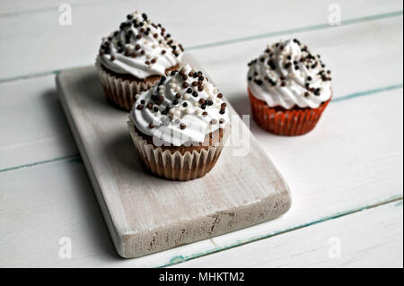 Vanille Cupcakes mit Butter Creme mit Schokolade Topping auf einem hölzernen Schneidebrett auf einem hellen Hintergrund Stockfoto