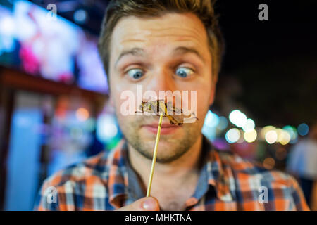 Kaukasischen jungen männlichen essen Kricket in der Nacht Markt in Thailand. Stockfoto