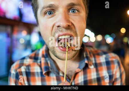 Kaukasischen jungen männlichen essen Kricket in der Nacht Markt in Thailand. Stockfoto