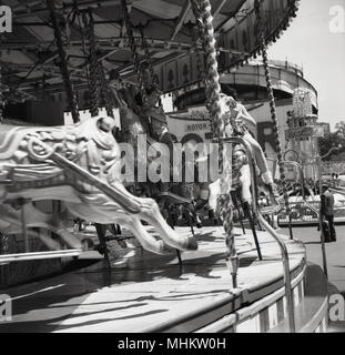 1960, historische, Kinder genießen eine Fahrt auf hölzerne Pferde auf einem traditionellen Karussell oder Merry-go-round an einem Sommertag an der Battersea Kirmes, London, England, UK. Stockfoto