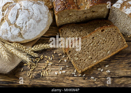 Gruppe von dunklen Brote mit Weizen, Sonnenblumen und Roggen Getreide auf einer hölzernen vintage Tabelle. Stockfoto