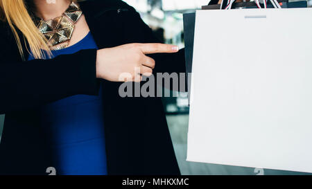 Die Frau zeigt mit dem Finger auf die Einkaufstasche, mit leeren Raum. Weiß Shopping Package, Kauf Konzept Stockfoto