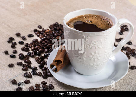 Schwarz Kaffee Tasse und Zimt auf Untertasse und gerösteten Kaffeebohnen im Hintergrund. Selektive konzentrieren. Essen und Trinken Konzept Stockfoto