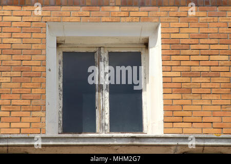 Ein altes Fenster mit Holzrahmen, braucht eine Renovierung auf einem Brick House Stockfoto