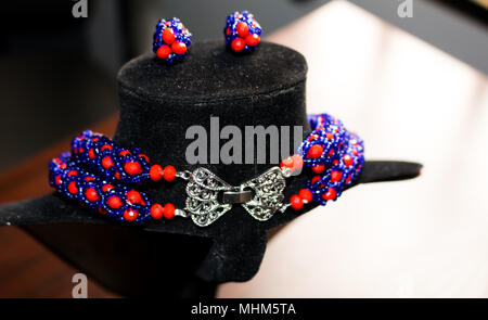 Handgefertigte Kette aus roten und blauen Perlen mit einer goldenen Brosche, passende Ohrringe Silber Spange auf einem schwarzen Mannequin Stockfoto