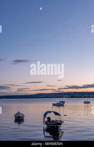 Kleine Boote auf dem See in der Abendsonne mit dem Mond im Hintergrund Stockfoto