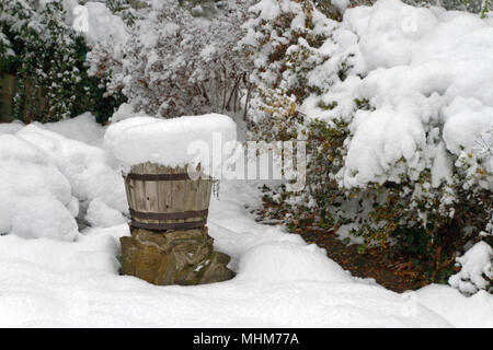 Eine Terrasse mit Gartenmöbeln, Pflanzer, Töpfe, Regenschirm und Garten Vegetation stark von einer tiefen Schnee im Winter Stockfoto