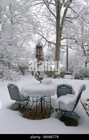 Einen Hinterhof deck mit Möbeln, Pflanzer, Töpfe, Regenschirm und Garten Vegetation stark von einer tiefen Schnee im Winter Stockfoto