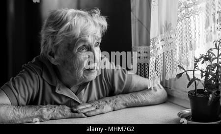Eine ältere Frau sieht traurig aus dem Fenster. Stockfoto