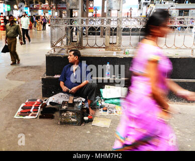 Ein Schuster sat beobachten, die Pendler auf die bahnhofshalle im CST, Mumbai, Indien Stockfoto