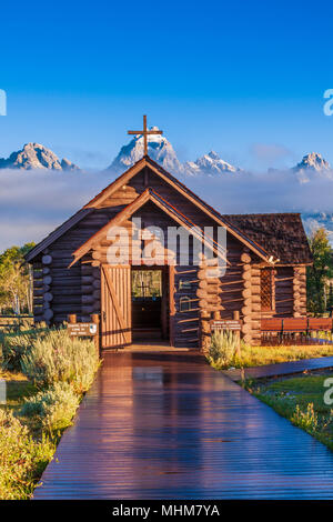 Grand Teton Bergkette und den bischöflichen Kapelle der Verklärung bei Sonnenaufgang, am frühen Morgen Licht getaucht mit Nebel und tiefliegenden Wolken. Stockfoto