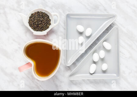 Herz geformte Becher, grüner Tee und Mandeln in weißer Schokolade auf Marmor Hintergrund. Stockfoto