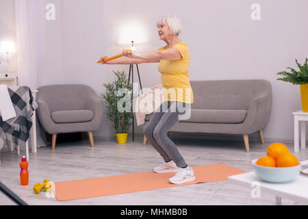 Athletische senior Frau hockt mit Gesundheit Zauberstab Stockfoto