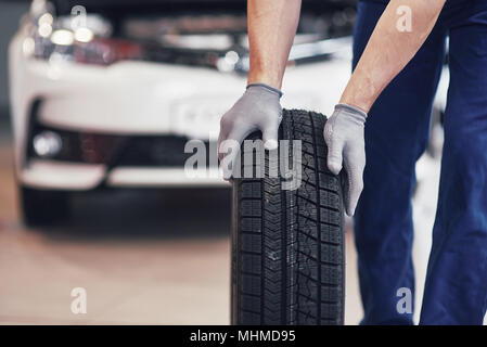 Mechaniker mit einem Reifen in der Werkstatt. Austausch des Winter- und Sommerreifen Stockfoto