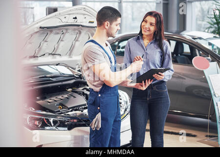 Mechaniker zeigen eine Papier in einer Zwischenablage zu einer Frau in einer garage Stockfoto