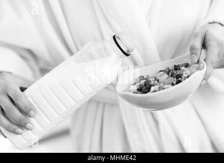 Closeup auf Frau gießt Milch in Platte mit Haferflocken Stockfoto