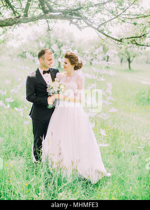 Die vertikale Sicht auf das glückliche Brautpaar steht auf der Vorderseite des Papiers Schwäne hängt am Baum. Stockfoto