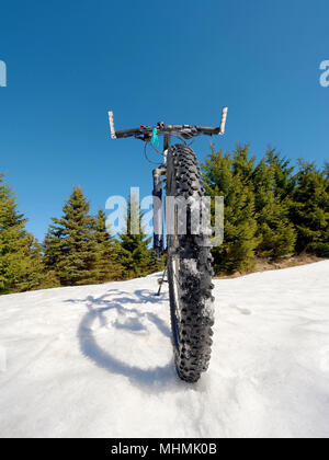 Schließen breiten Ansicht Mountainbike bleibt im Schnee. Winter schneebedeckte Berge mit der Straße zwischen den Bäumen. Stockfoto