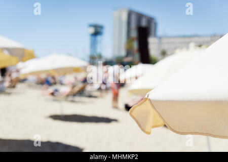 Nahaufnahme von einigen beige Sonnenschirme in La Barceloneta Beach, in Barcelona, Spanien, mit unkenntlich Menschen Sonnenbaden im Hintergrund Stockfoto