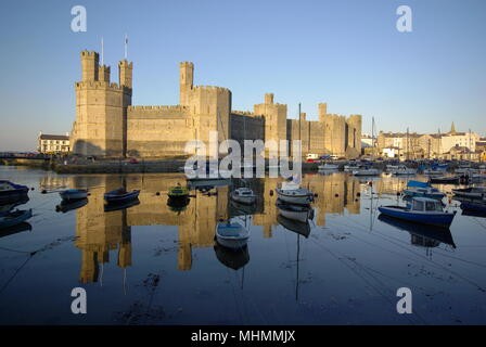 Ein beeindruckender Blick auf Caernarfon (Caernarvon) Castle in Gwynedd, Nordwales, mit zahlreichen Booten auf dem Wasser im Vordergrund. Die Burg wurde von dem englischen König Edward I. aus dem Jahr 1283 an der Stelle einer römischen Festung und Norman motte erbaut. Stockfoto