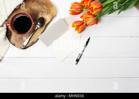 Overhead Schuss ein Bouquet von Orange und gelbe Tulpe Blumen mit schwarzen Kaffee, leere Karte mit textfreiraum und eine gemütliche Decke über weißen Strick woo Stockfoto