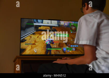 Ein teenager Boy spielt die Hit computer spiel Fortnite auf einem großen TV auf einer Playstation 4-Konsole. Stockfoto