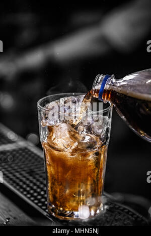 Gießen Cola in das Glas voller Eiswürfel Stockfoto