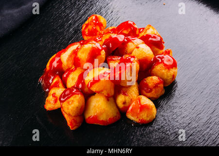 Typisch spanische Speisen, Patatas Bravas, Bratkartoffeln mit einer heißen Sauce, auf einem dunklen Hintergrund Stockfoto