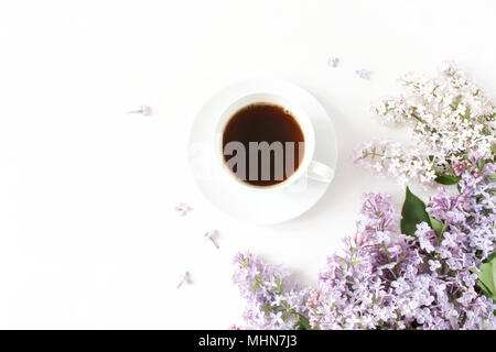 Blumige Komposition aus schönen lila Flieder, syringa Blumen auf weißem Holz- Hintergrund mit Tasse Kaffee. Feminine Büro Schreibtisch, eingerichteten Lager Bild, Flach, Ansicht von oben mit der leere Raum. Stockfoto