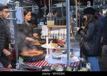 Eine Frau wählt Essen vom Markt Anbieter im Old Spitalfields Market, in Tower Hamlets, Spitalfields, London, Großbritannien, 29. Oktober 2017. () Stockfoto