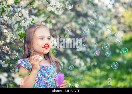 Kleine Mädchen bläst Seifenblasen in Cherry Blossom garden Stockfoto