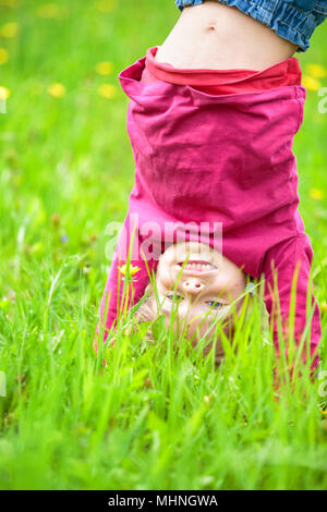 Glückliche kleine Mädchen stehen auf dem Kopf stehend auf dem Rasen im Sommerpark Stockfoto