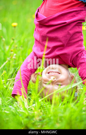 Glückliche kleine Mädchen stehen auf dem Kopf stehend auf dem Rasen im Sommerpark Stockfoto