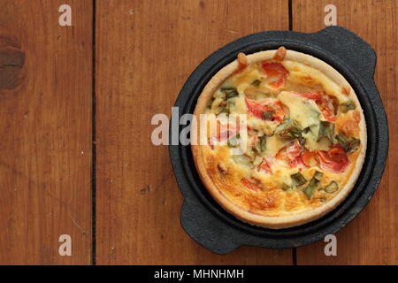 Tomaten und Frühlingszwiebel quiche in einem gusseisernen Topf, Teller auf einem Holz Hintergrund Stockfoto