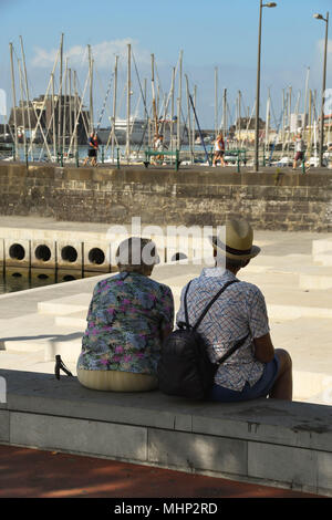 Der Mann und die Frau auf einer Bank unter dem Schatten eines Baumes in Funchal, Madeira, mit Marina der Stadt im Hintergrund Stockfoto